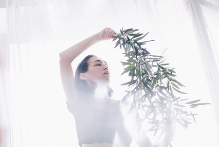 girl holds a branch of olive tree in sunlightの写真素材