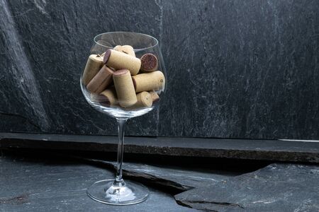 Wine glass filled with corks on dark gray stoneの写真素材