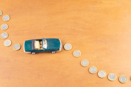 Toy car on coin road on a wooden backgroundの写真素材