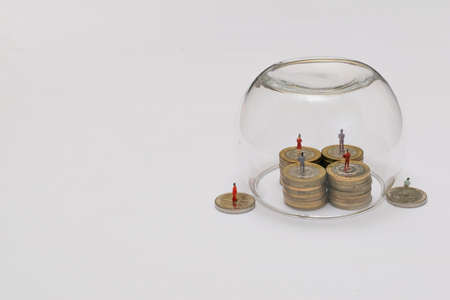 Miniatures of people on a pile of coins protected by glass bubbleの写真素材