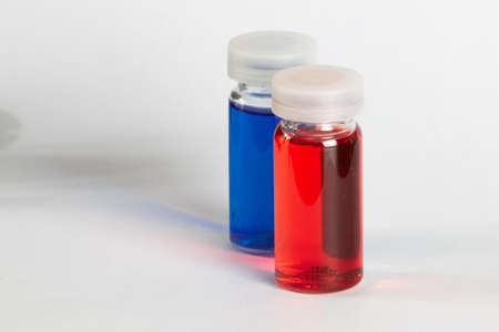 Two small transparent containers with red and blue liquid on white backgroundの写真素材
