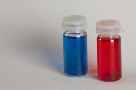 Two small transparent containers with red and blue liquid on white backgroundの写真素材