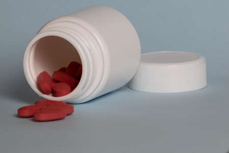 White medicine package with red tablets inside and outside on a light blue backgroundの写真素材