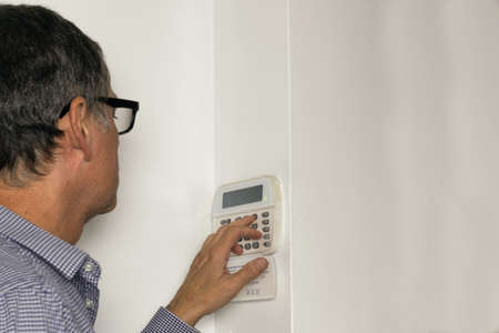 Man with glasses on an alarm keypad on a white wallの写真素材