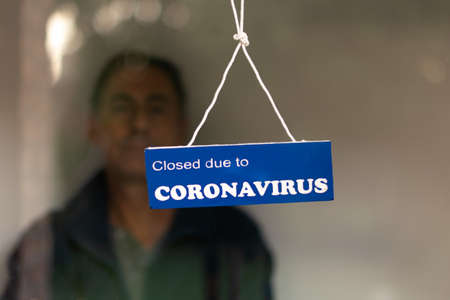 Man behind the door of a closed business behind a closed for coronavirus signの写真素材