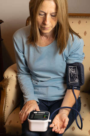 Woman taking her blood pressure with an electronic device at homeの写真素材