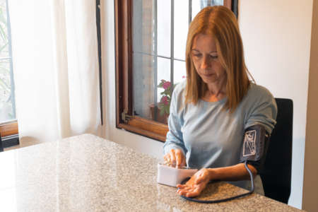 Woman taking her blood pressure with an electronic device at the homeの写真素材