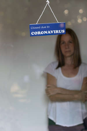 Woman behind the window of her business closed by covid indicate by a signの写真素材