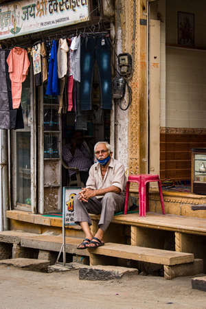 Jaisalmer, Rajasthan / India - july 22 2020 : bored old man sitting outside of his shop wearing mask not fully covered.のeditorial素材