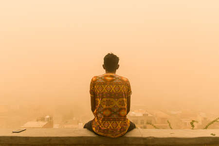 man sitting on the wall facing city enjoying the view in the middle of the sandstormの写真素材