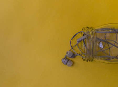 grey color earphone in a glass jar on a yellow background, conceptual image.の写真素材