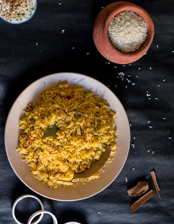 Cooked spicy rice on a plate with some of the ingredients on a black background. Hot spices, raw rice Cooked rice, curd. Healthy recipe, top viewの写真素材