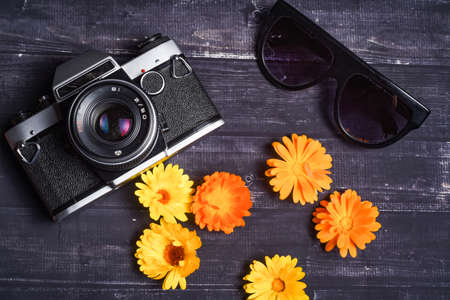 Travel concept. Summer flowers, camera, sunglasses on dark wooden background. Top view