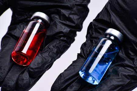 Concept of choice treatment. Close up Doctor hands holding two ampoules. Medical ampoules with liquid. Red and blue ampoules.の写真素材