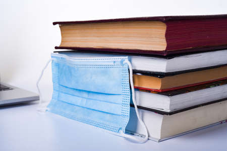 A medical or surgical mask on a stack of books. Medical mask and a stack of books on a white background. With space for letters or text. Quarantine and self-isolation conceptの写真素材
