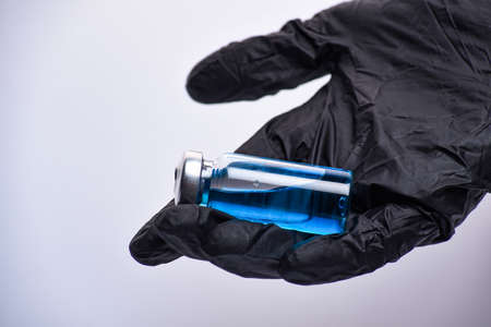 A woman's hand in black gloves holds an ampoule. Vaccine. The ampoule with the medicine. Medication for injection.の写真素材