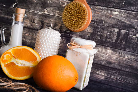 The lay composition with body care products and space for text on dark wood background. a jar of natural cream, a bottle of coconut oil and a ripe orange and candleの写真素材