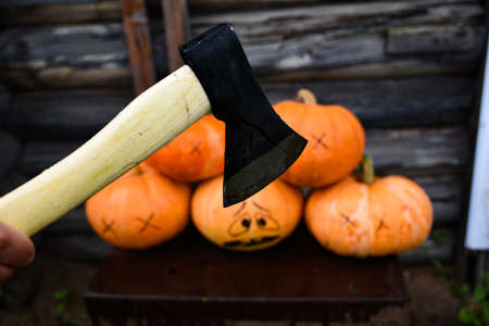 halloween concept. Pile of pumpkins with an ax for chopping. Horror scene of the group of dead pumpkins and one pumpkin is afraid of a hand with an ax. Hand with an ax kills pumpkins.の写真素材
