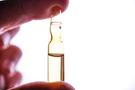 A woman's hand holds an medical vial or ampoule. Vaccine. The ampoule with the medicine. Medication for injection.の写真素材