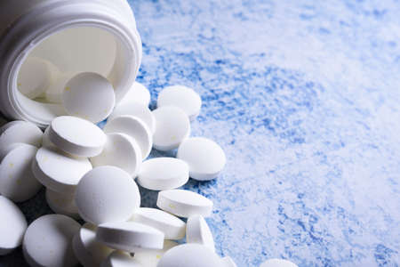 White medical pills and tablets spilling out of a drug bottle. Macro top down view with copy space.の写真素材