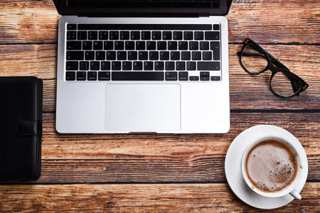 laptop, glasses and a cup of coffee on a wooden table top view. Vacation or online learning conceptの写真素材