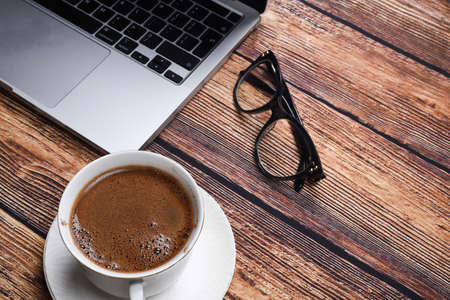 laptop, glasses and a cup of coffee on a wooden table top view. Vacation or online learning conceptの写真素材