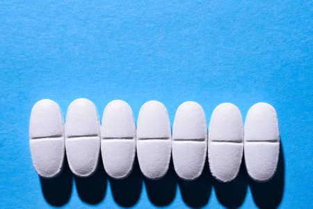 many white medical pills in a row on a blue background. pills cast a shadow. Copy spaceの写真素材