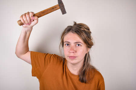 woman in brown T-shirt, holding hammer, looking at camera, isolated on white background. home renovation conceptの写真素材