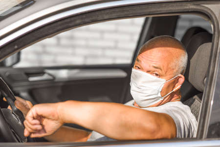 Senior man in medical mask driving a car, looking at the camera. coronavirus concept. respiratory protectionの写真素材