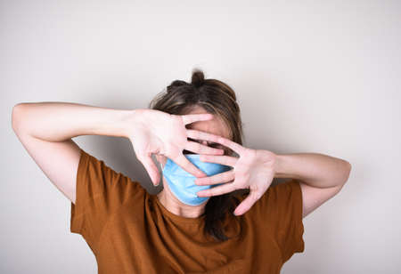 Scared woman in medical mask covers her face with her hands, isolated on white backgroundの写真素材