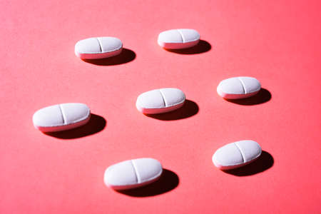many white medical pills in a row on a pink background. pills cast a shadow. pill pattern. Copy...