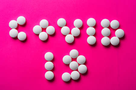 inscription COVID 19 from many white pills on a pink background. accept gifts concept. Cardiology or love conceptの写真素材