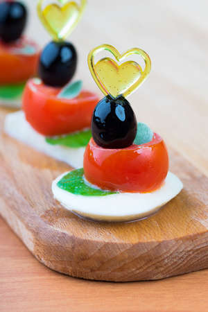 Simple snack canape with tomato, mozzarella and basil close-up on wooden backgroundの写真素材