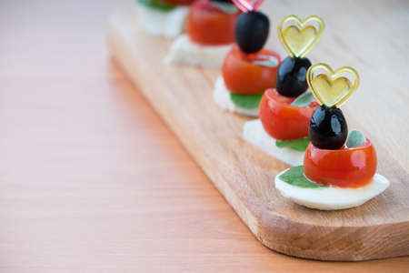 Simple snack canape with tomato, mozzarella and basil close-up on wooden backgroundの写真素材