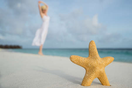 woman in a white dress dancing on the tropical beach against starfish closeupの写真素材
