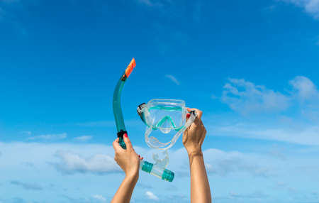 Hand holding snorkel goggles   mask for diving  against beach and skyの写真素材