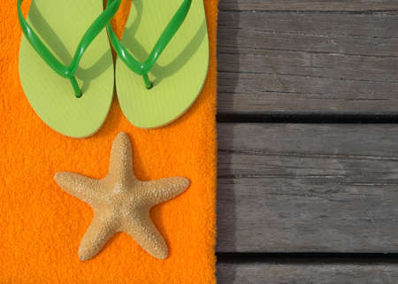 Beach slippers, towel and starfish on wood background. Concept of leisure and travelの写真素材