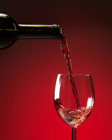 Red wine being poured into wine glass on red backgroundの写真素材