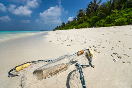 Message in a bottle washed ashore on a tropical beach.の写真素材