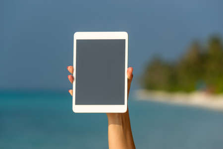 Concept of internet and communication. blank empty tablet computer in the hands of women on the beachの写真素材