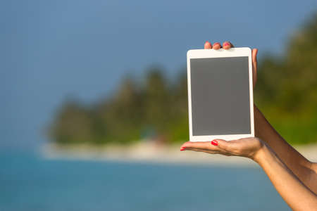 Concept of internet and communication. blank empty tablet computer in the hands of women on the beachの写真素材