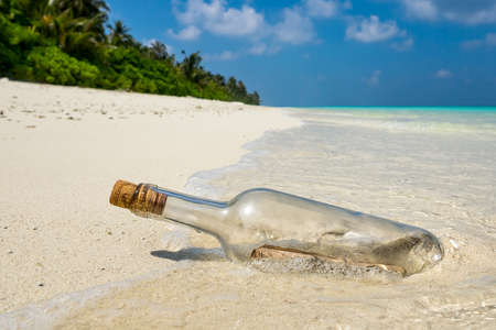 Message in a bottle washed ashore on a tropical beach.の写真素材