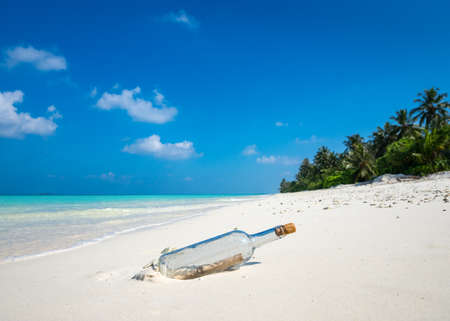 Message in a bottle washed ashore on a tropical beach.の写真素材
