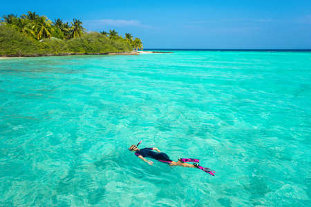Woman snorkeling in clear tropical waters in front of exotic islandの写真素材