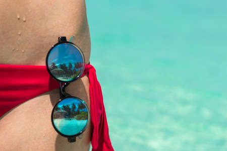 Close-up of hot and seductive lady with perfect figure in magenta panties posing over sea background with sunglasses.の写真素材