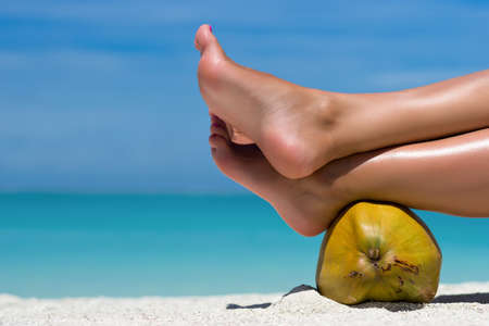 Female feet propped on coconut on the beach, blue sea background