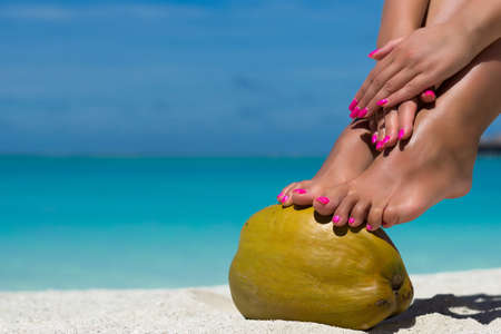 Female feet propped on coconut on the beach, blue sea background
