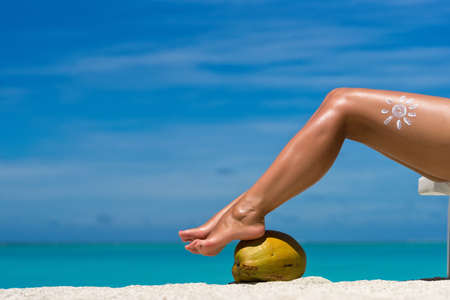 Women's beautiful legs on coconut on the beach, blue sea backgroundの写真素材