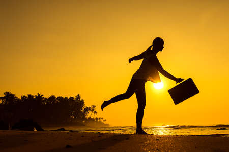 Female Silhouette staying along Ocean Coast with Luggage Bag enjoying scenic View Sea and Sunrise on background. Beach Holiday Concept.の写真素材