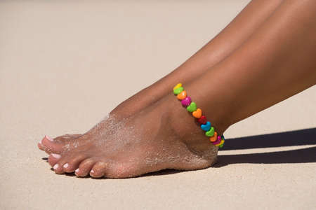 Beach travel - woman seated on sand beach. Closeup detail of female feet